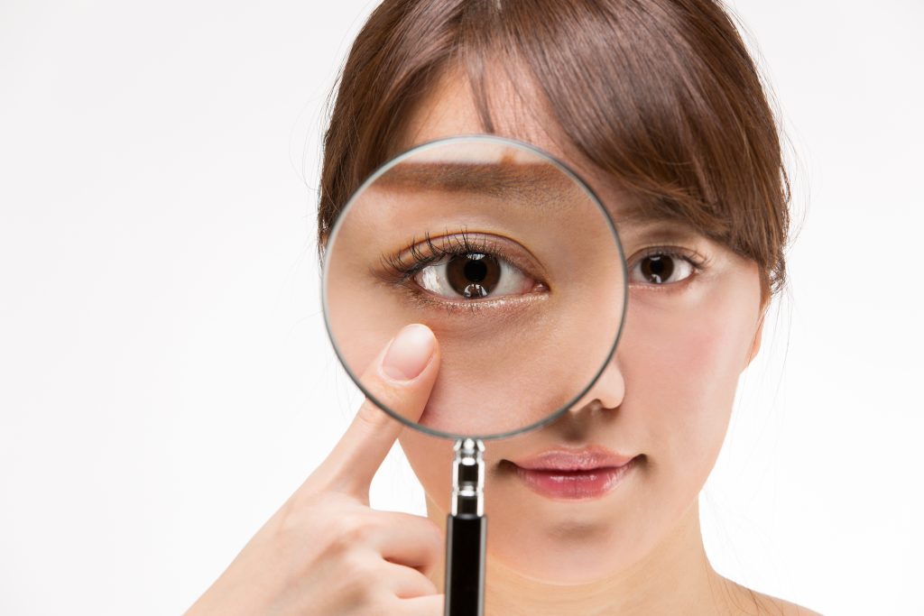 虫眼鏡で目を拡大している女性